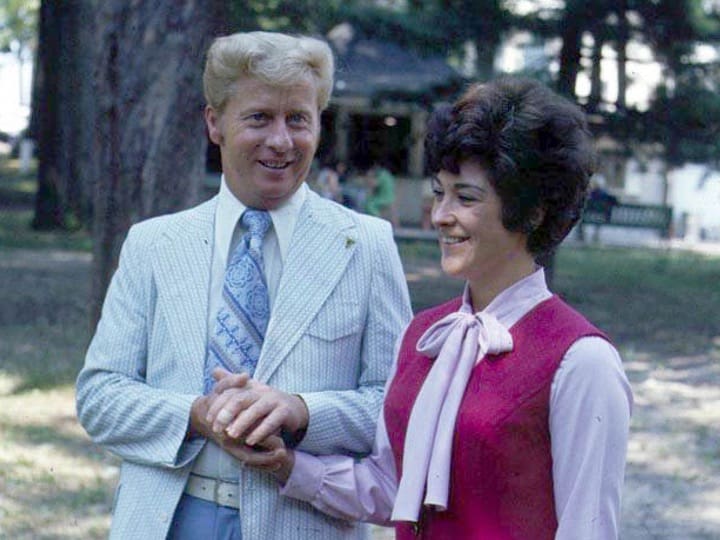 Smiling man and woman outdoors, holding hands.